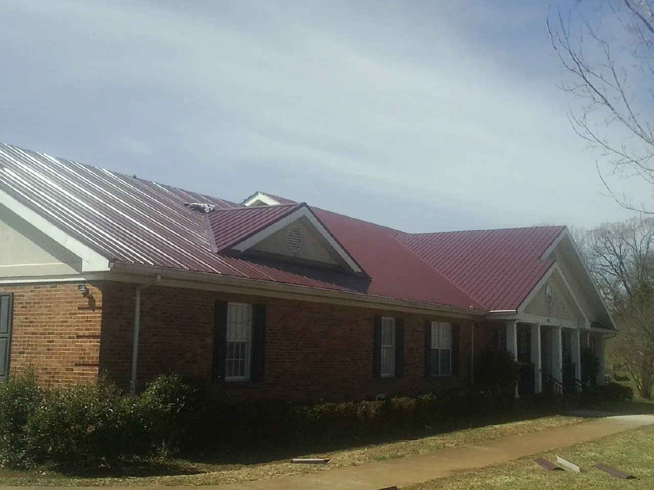 Red metal roof with gabled entries on a long brick building, from a Hail Damage Roof Repair job in Channahon