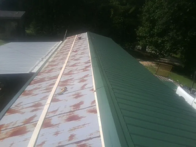Old rusted panels beside newly installed green metal roofing in Channahon