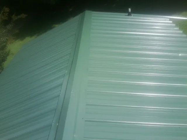New green metal panels meeting at the ridge of a roof — Flat Roof Repair work by our crew in Channahon