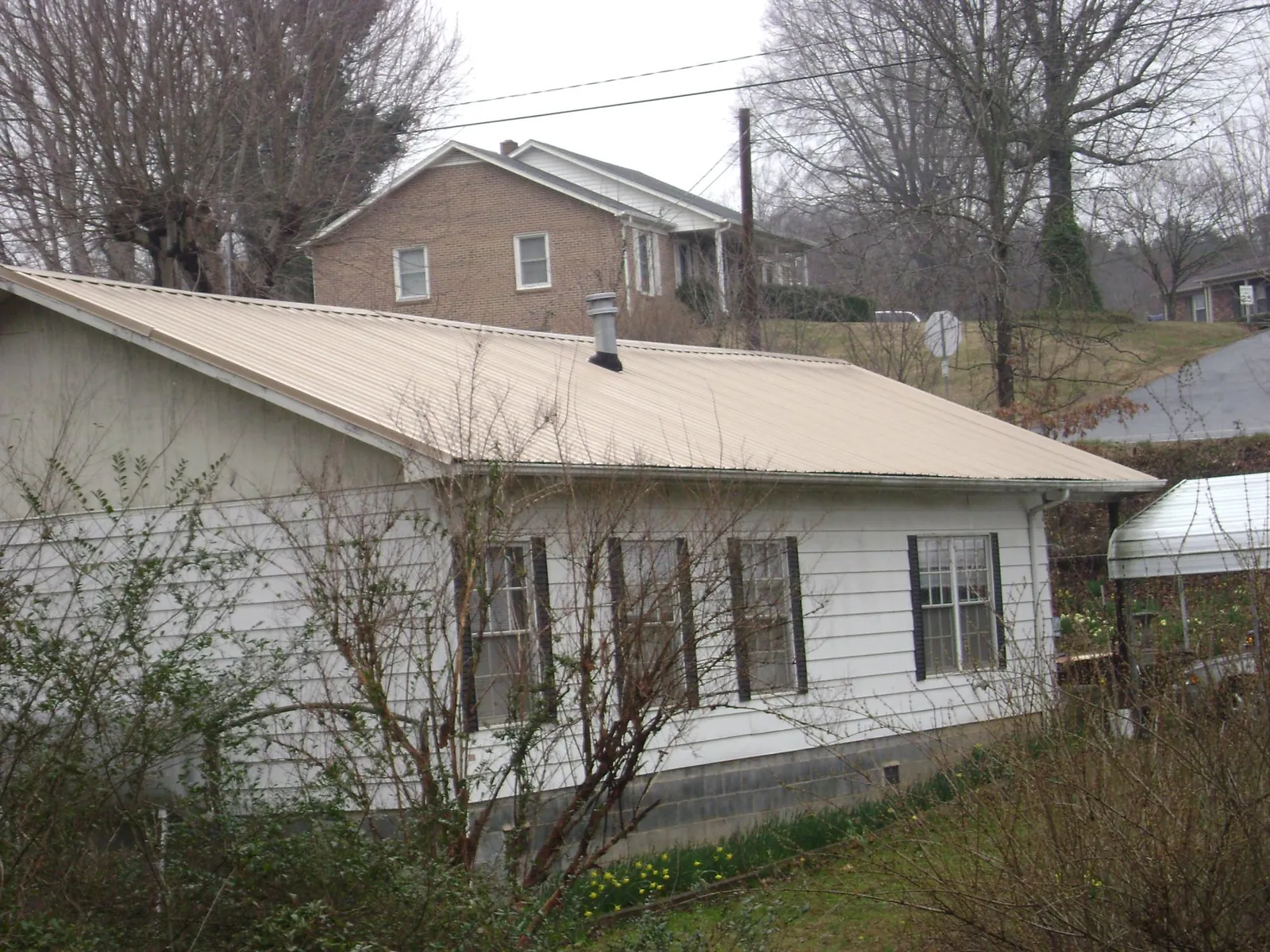 Tan metal roof on a white sided house set into a hillside — Commercial Roofing by Roofing Brothers in Channahon
